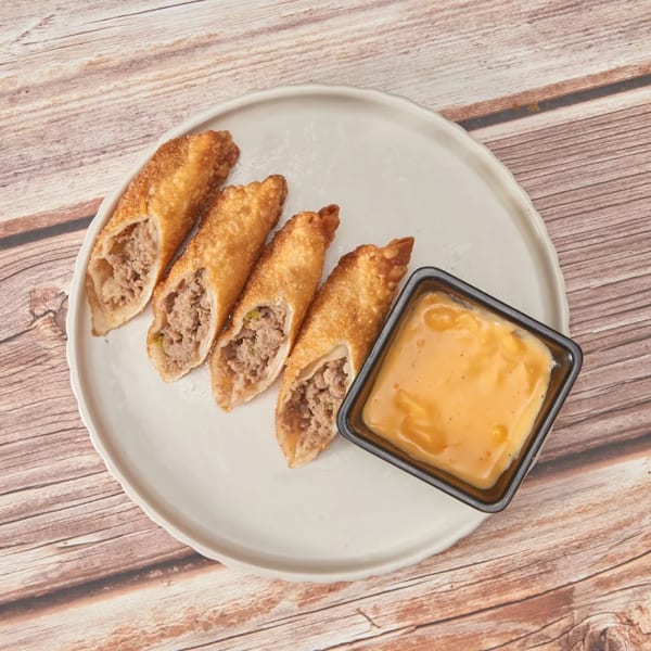 Four crispy egg rolls filled with ground meat, served with a side of orange dipping sauce.