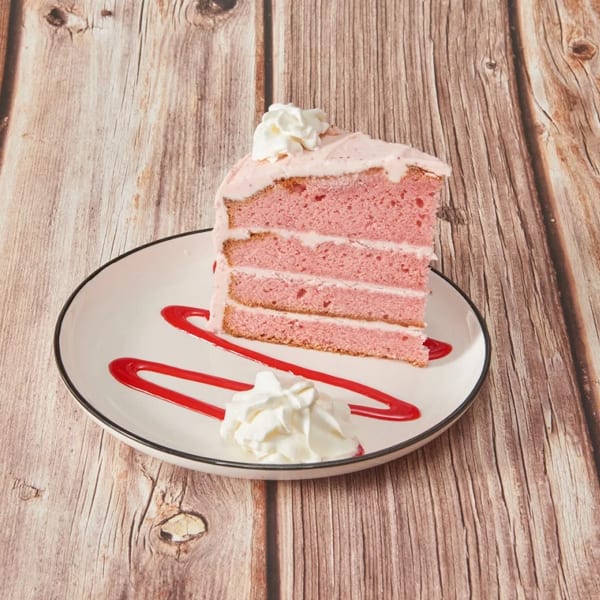 A slice of pink layer cake with white frosting and whipped cream on a white plate.